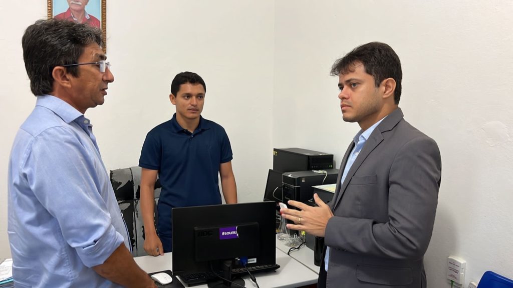 Na imagem: Dr. Danilo Rocha está conversando com dois senhores, em uma sala. 